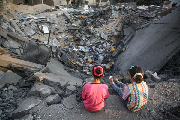 Två palestinska barn med ansiktena vända från kameran tittar på en förstörd byggnad, 9 augusti 2022.